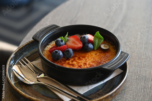 Fotografie French crème brûlée dessert with fresh fruit served in a black bowl