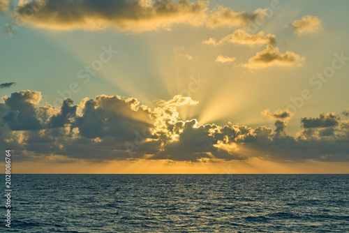 Tableau sur toile Golden sun rays breaking through clouds over ocean