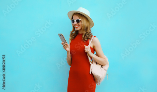 Beautiful happy young woman smiles with mobile phone looking at smartphone on blue background