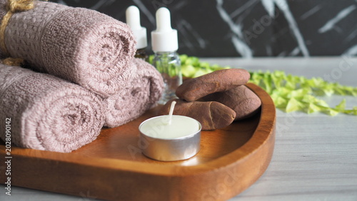 Photography Spa wellness composition with rolled towels, essential oil dropper bottles, massage stones and candle on wooden tray