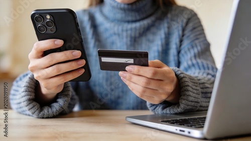 Woman holding credit card and smartphone while shopping online near laptop computer illustrating secure payment method e-commerce transaction and digital banking for internet