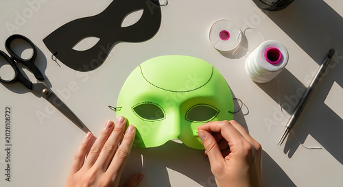 Hands crafting a lime green mask with black paper mask and sewing supplies