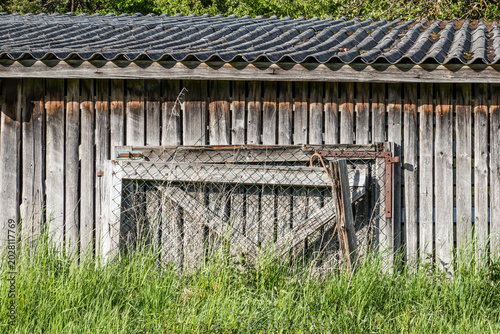 Abandoned Weathered Wooden Barn with Corrugated Roof and Rusty Wire Fence, Rural Decay