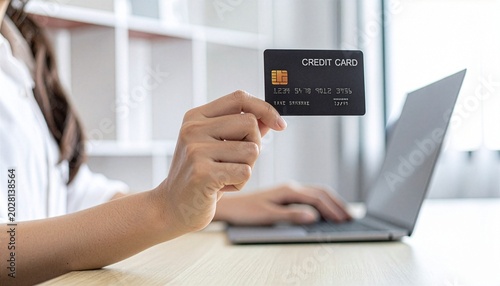 A person's hand holds a credit card over a laptop keyboard, suggesting online shopping or financial transactions.