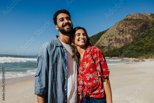 Sunlit closeness: A couple leaning into each other by the sea
