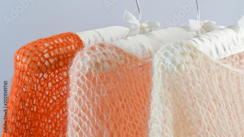 Fotografie Knitted mohair sweaters hanging on white hangers.