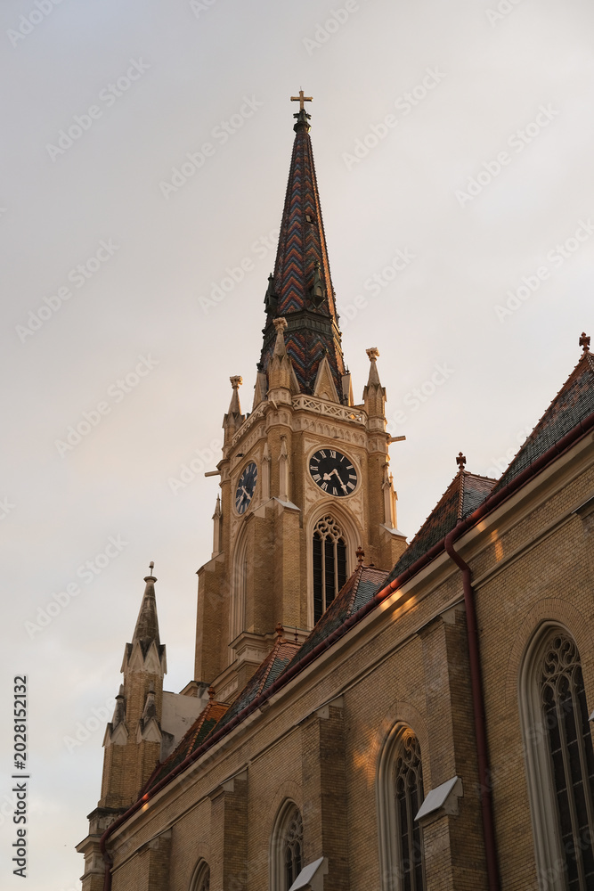 Fototapeta premium Church tower and steeple with clock, gothic brick architecture, daylight sky, ornate exterior of historic religious building