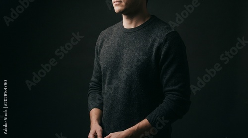 A man wearing a dark sweater stands against a black background.