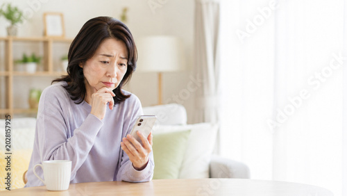 スマホを見ながら不安そうに考える中高年女性