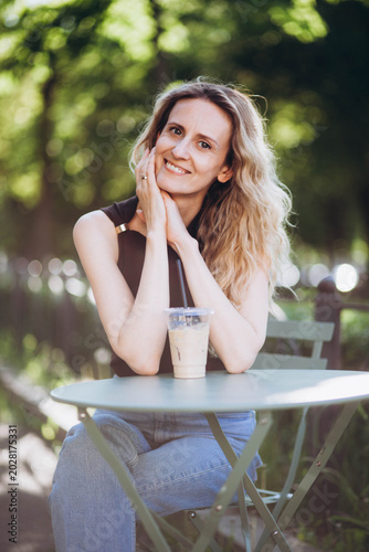 A young woman is drinking coffee at a table in the park.