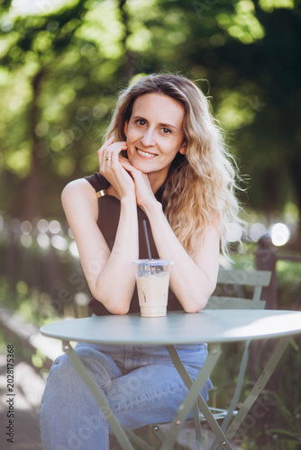 A young woman is drinking coffee at a table in the park.