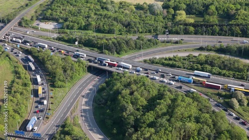 Aerial perspective of a multi-lane motorway interchange filled with heavy traffic. Cars and trucks are bumper to bumper on congested roads during bright daytime.