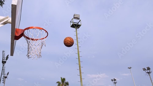 Slow motion footage of a basketball perfectly swishing through the hoop on a beautiful spring day. Blue sky, soft clouds, and the movement of the net create a dynamic and cinematic sports atmosphere. 