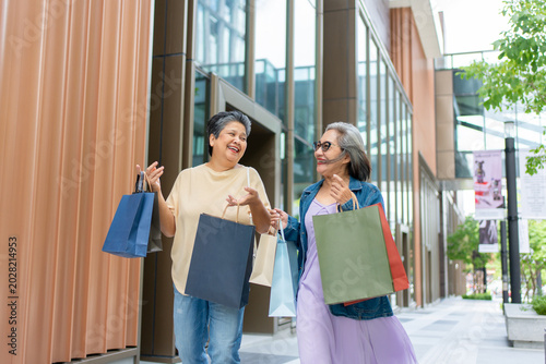 Quadro su tela Two happy Asian senior women walking outdoors with shopping bags