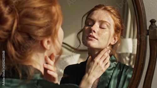 Young redhead woman looking at her reflection in bedroom mirror