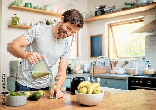 Obraz na plátně Earphones, man and pour green smoothie in home for breakfast shake, healthy diet and happy