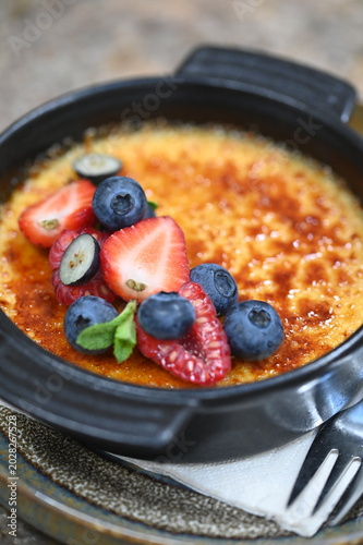 Fotografie French crème brûlée dessert with fresh fruit served in a black bowl