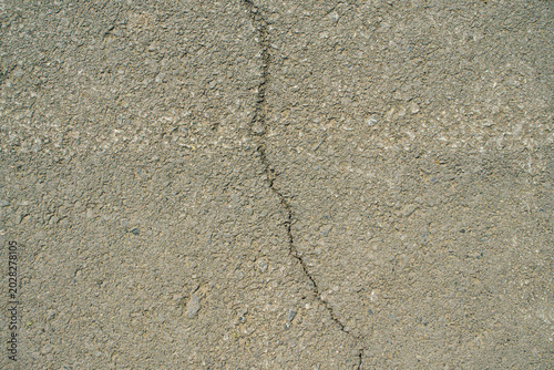 A top-down close-up shot of an uneven grey asphalt surface featuring a continuous vertical narrow crack