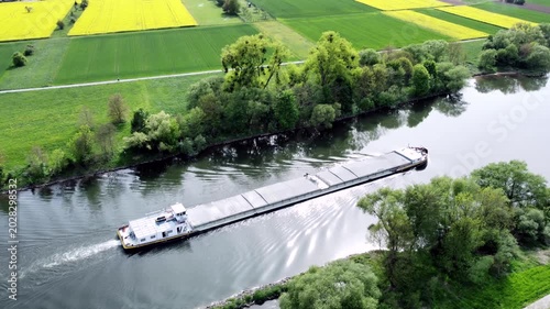 Drohne fliegt über Fluss mit Binnenschiff, Ufer mit Auwald und Agrarland, Luftaufnahme