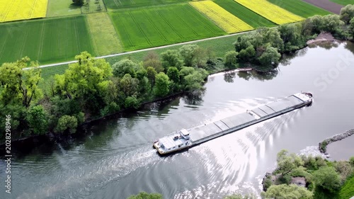 Drohne fliegt über Fluss mit Binnenschiff, Ufer mit Auwald und Agrarland, Luftaufnahme