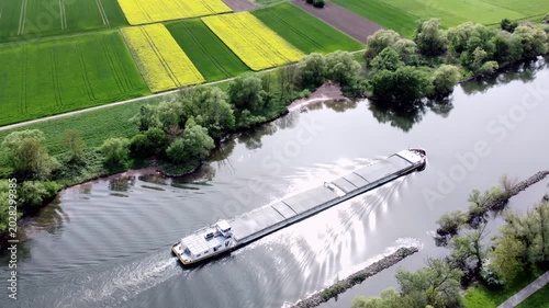 Drohne fliegt über Fluss mit Binnenschiff, Ufer mit Auwald und Agrarland, Luftaufnahme