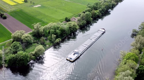Drohne fliegt über Fluss mit Binnenschiff, Ufer mit Auwald und Agrarland, Luftaufnahme