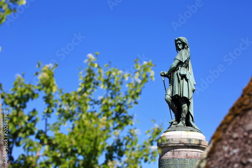 Foto Das historische Vercingétorix-Monument von der Seite auf seinem Sockel, umrahmt von grünen Blättern vor einem wolkenlosen, tiefblauen Himmel