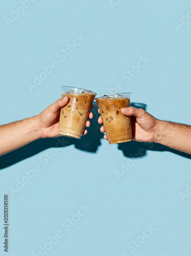 Iced coffee drinks held by hands toasting against vibrant blue background, celebrating summer refreshments.