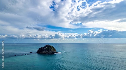 Isolated, rocky island in calm turquoise sea under a cloudy blue sky