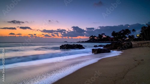 A tranquil beach scene at dusk, featuring long exposure waves and palm trees silhouetted against a colorful sky