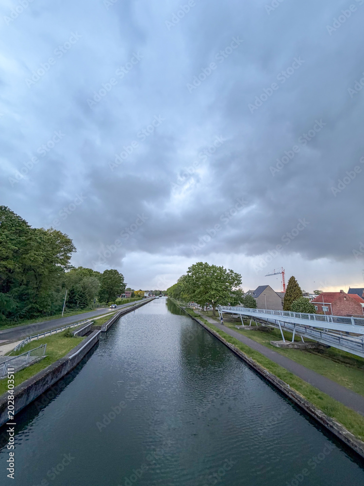 Fototapeta premium Peaceful canal waterway with bridge at dusk in Rijkevorsel, Turnhout region, België - moody evening landscape with cloudy sky