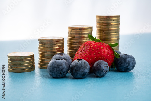 Strawberries and blueberries near piles of coins. Rising prices of fruit and groceries.