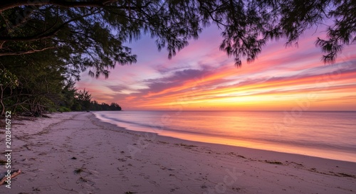 Wide sandy beach under vibrant purple and orange sunset.