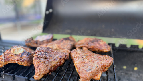 Close-up of juicy ribs on a charcoal grill grate outdoors, meat with a ruddy crispy crust, concept of barbecue, picnic in nature and summer recreation with fried meat.