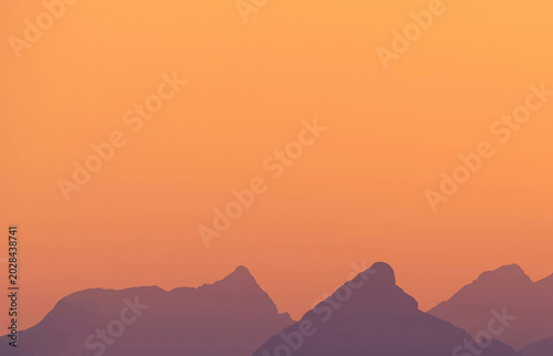 Silhouette of mountain peaks against a gradient orange sky during sunset