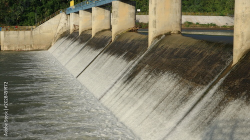Fotografie Water rushes over a concrete dam under cloudy skies