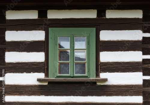 Old green wooden window on dark brown log wall of traditional rustic country cottage