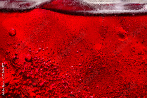 Fotografia Macro shot of cold red drink with condensation droplets on glass,Close-up macro texture of a refreshing cold red beverage in a glass, covered with condensation water droplets and small ice bubbles