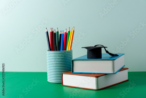 Canvastavla A miniature graduation cap on a stack of books next to a container of colored pencils