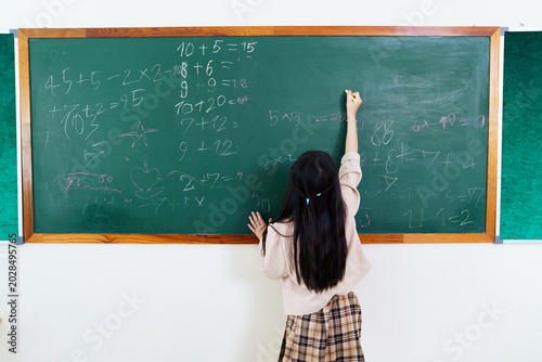 Young Asian girl solving math problem on blackboard
