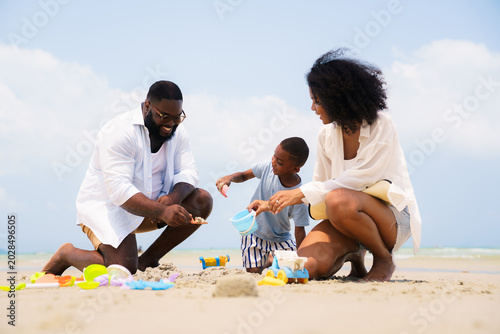 Happy Black family building sandcastle together on beach