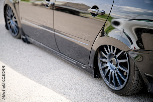 Fotografi Detail of a modified black vehicle with dropped suspension parked on a street