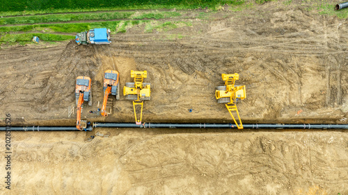 Aerial view of a major pipeline construction project. Heavy machinery including excavators and pipelayers install a new gas line in a rural field. Industrial energy infrastructure development.