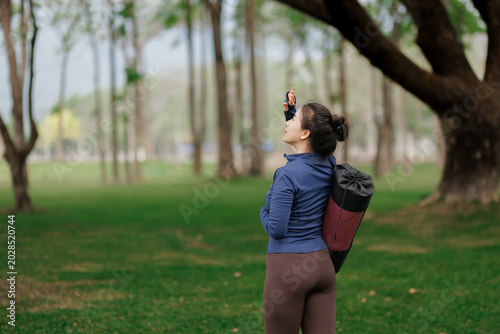 Schilderij op canvas Sporty woman carrying her yoga equipment in a public garden.
