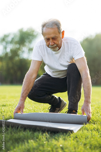Senior man preparing for or finishing outdoor yoga session. Concept of healthy aging, wellness, and active lifestyle