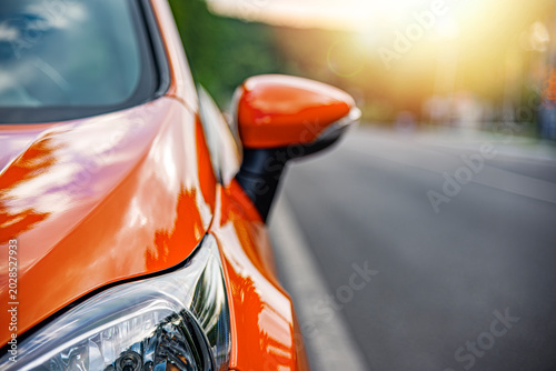 A bright orange car parked on the side of a city street during a sunny day.
