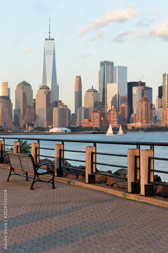 Obraz premium Serene Waterfront Scene. Calm Lakeside With Empty Benches And Sailboats Nearby new york