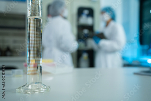 Glass Measuring Cylinder in Focus with Scientists Working in Blurred Laboratory Background