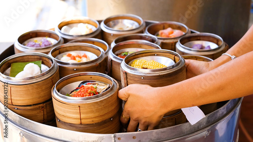 Obraz na plátně Hands Selecting Various Steamed Dim Sum in Bamboo Baskets at Phuket Market