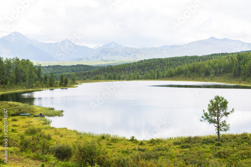 A figure of a fisherman in a boat and a picturesque Lake Kodelyukyol in Ulagan region in summer in Altai. Ulagan, Altai, Siberia, Russia 